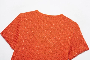 Detail of orange knitted top featuring shimmering sequins and round neckline texture