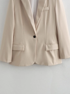 Close-up detail of beige blazer featuring a single black button and classic flap pockets