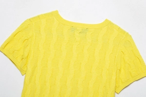 Detailed view of the bright yellow knit top showing textured cable wave pattern and crew neck