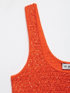 Detail of bright orange knit top showing intricate texture and shimmering sequins