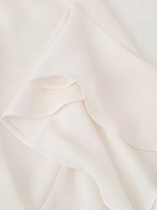 Dettaglio dei bordi a balze su una camicetta di chiffon crema con cuciture sottili