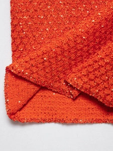 Macro detail of vibrant orange knit fabric with shimmering gold sequins and texture