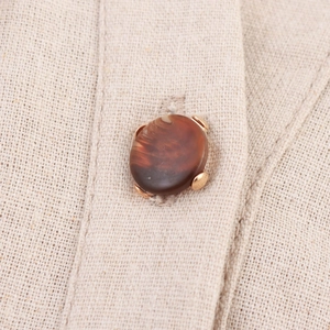 Detail of brown marble button with gold metal claws on beige linen shirt dress