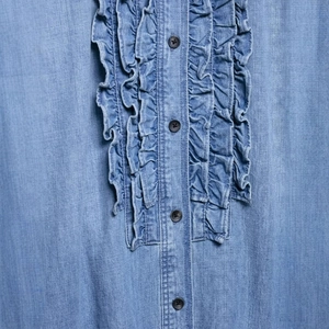 Close-up of light blue denim shirt with ruffle trim details and black buttons