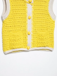 Dettaglio del gilet all'uncinetto giallo e crema con grandi bottoni ovali e trama a maglia