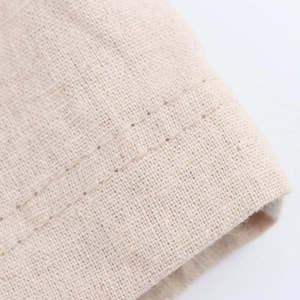 Macro shot of double-row stitching detail on the beige cotton-linen fabric of the dress