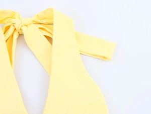 Detail of elegant yellow halter neck dress featuring a large bow knot and textured fabric