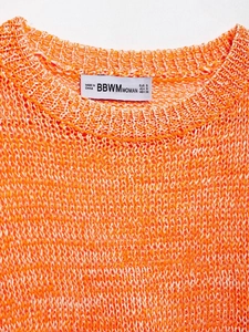 Close-up detail of the crew neckline and woven fabric texture on an orange knit sweater