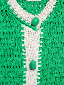 Dettaglio ravvicinato del cardigan verde erba con bordi bianchi e bottoni in resina