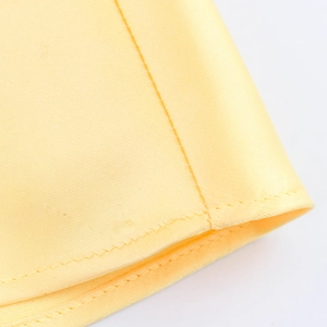 Detail shot of high-quality yellow satin fabric with precise stitching on dress hem