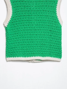 Dettaglio del gilet in maglia crochet verde con bordo a coste crema e motivi geometrici