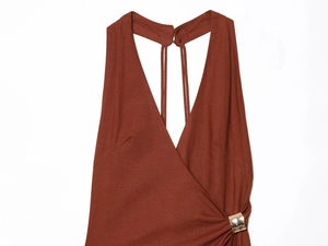 Detailed close-up of golden metal ring and side pleats on a terracotta halter dress