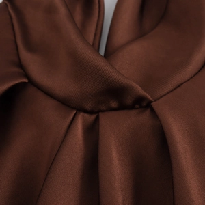 Detail of the elegant dark brown satin dress showing refined pleats and knotted silk texture