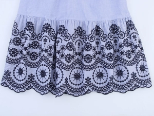 Detail of blue striped dress hem featuring navy floral embroidery and scalloped lace edges