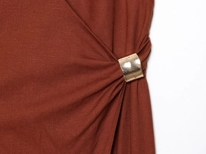 Detail view of brick red dress waist with elegant gold metal buckle and pleated design