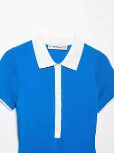 Dettaglio della polo in maglia blu con colletto bianco ed etichetta del marchio sul collo
