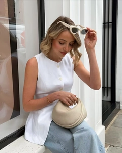 Detail of light beige pleated half-moon handbag in grained leather held by a model