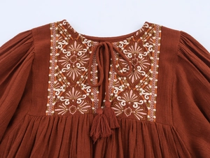 Close-up of rust-red linen dress with bohemian embroidery and tasseled neck ties
