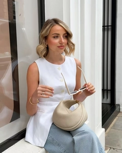 Chic beige half-moon leather handbag styled with a sleeveless vest and denim pants