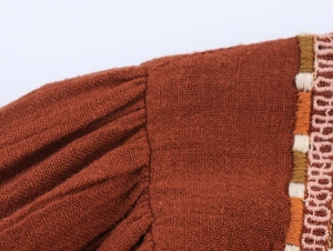 Close-up of brick red linen fabric featuring intricate hand-woven embroidery and smocked pleats