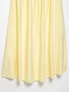 Detail of light yellow summer dress showing draped fabric texture and pleated hemline