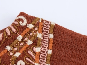 Detail of bohemian floral embroidery on dark brown linen fabric with intricate stitching
