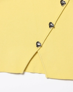 Détail du tissu tricoté jaune clair avec bord superposé et boutons en métal argenté