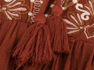 Close-up of bohemian floral embroidery and tassels on rust-red textured cotton dress
