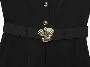 Détail d'une combinaison noire avec une grande boucle fleur dorée et boutons en métal