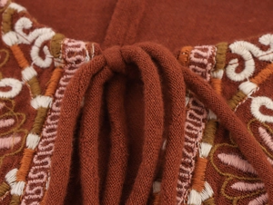 Close-up of ethnic embroidery and drawstring tassels on a rust-red cotton-linen dress