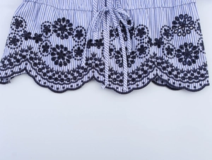 Detail of blue striped dress featuring dark floral embroidery and wavy lace hem