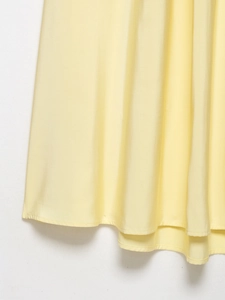 Detailed close-up of light yellow dress hem showing silk-like texture and fine stitching