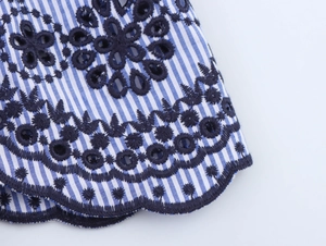 Detail of blue striped fabric with navy floral embroidery and scalloped eyelet edge