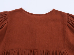 Detail of rust red cotton linen dress showing round neck and pleated puff sleeves