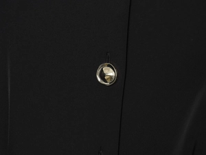 Détail d'un bouton métallique ondulé unique sur un tissu de combinaison noir