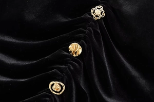 Detailansicht von luxuriösem schwarzem Samtstoff mit eleganten goldenen Zierknöpfen