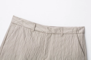 Detail view of beige pleated fabric shorts featuring vertical stripes and waistband pockets