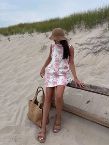 Detail of floral print mini dress with straw hat and canvas tote bag on the beach