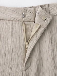 Macro detail of khaki striped trousers featuring zipper fly and hidden metal hook closure