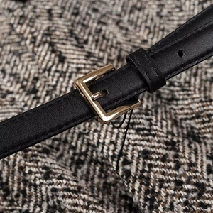 Close-up of black leather waist belt with golden square buckle on grey tweed fabric