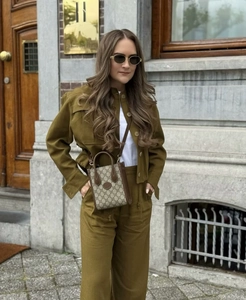 Detail of olive green utility jacket with drawstring waist and designer monogram crossbody bag