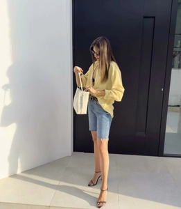 Detail of light yellow striped long sleeve shirt with blue denim shorts and white handbag