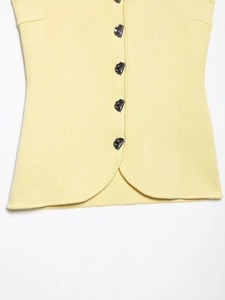 Detail of light yellow knit vest with irregular silver buttons and curved hemline