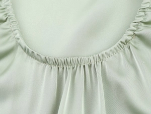 Detailed close-up of pale green satin dress showing fine pleats and neat stitching