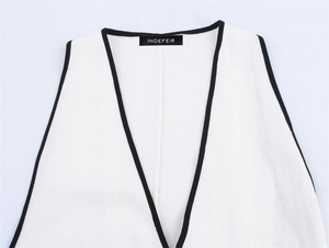 Close-up of V-neckline with black trim and brand label on white linen blend dress