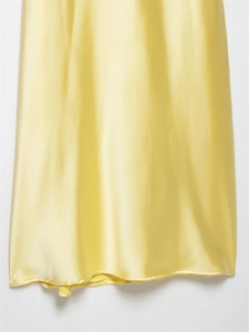 Close-up of light yellow satin dress hem showing smooth silk texture and fine stitching