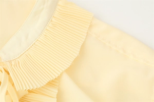 Makrodetail des plissierten Rüschenausschnitts an elegantem hellgelbem Chiffon-Set