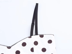 Detail of adjustable black straps and lace trim on a white polka dot satin top