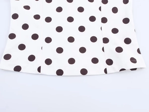 Close-up of the smooth hemline with classic black polka dots on white fabric garment