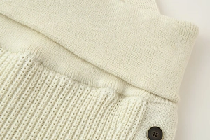 Detailed close-up of cream knit fabric showing ribbed textures and a vintage button